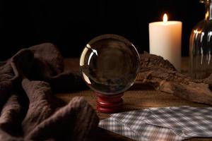 concept of fortune-telling on a wooden table and white candle with a crystal ball and tarot cards on dark background photo