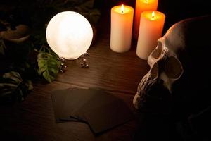 fortune-telling on a wooden table and a white candle with a crystal ball and cards on dark background. predict, prediction, horoscope, macabre, witchcraft, skull photo