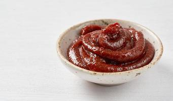 gochujang o coreano rojo chile pegar en un cerámico cuenco en blanco madera antecedentes. rojo chile salsa gochujang condimento foto