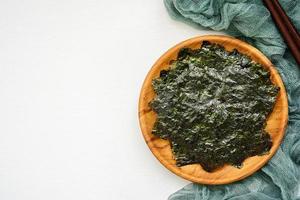 top view or flat lay roasted nori laver seaweed snack in wood plate on white wooden table background. nori laver seaweed crispy in wood plate on white wooden table background. overhead photo