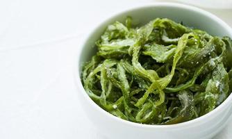 heap of fresh Korean salted seaweed salad stem side dish or Miyeok Julgi Bokkeum in white bowl on white background. Laminaria or Kelp Seaweed stem photo