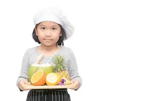 retrato de linda niña cocinero con mezcla frutas, naranja, Coco y piña y cocinar sombrero, delantal estar y sonrisa aislado en blanco antecedentes. foto