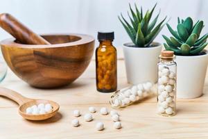 concept of homeopathic pills in a wooden spoon and bottles with a mortar with a pestle on wooden table background photo