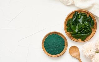 top view or flat lay laminaria or kelp seaweed and spirulina powder in wood plate and spoon background. spirulina powder with konbu and alga food on white table background. photo