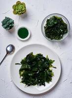 laminaria Kelp seaweed and spirulina powder with a ceramic bowl on white background. top view photo