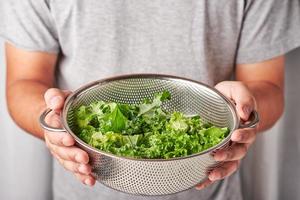 concept a healthy man with a hand holding a washing bowl colander of fresh organic kale. white curtain background photo