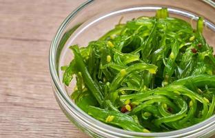 close up wakame seaweed salad with sesame seed in glasses bowl on wood table background photo