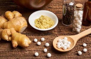 concept of homeopathic pills in a wooden spoon and bottles with herb on wooden table background photo