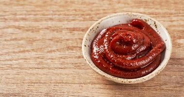 Gochujang or Korean red chili paste in a ceramic bowl on wood background. red chili sauce gochujang condiment photo