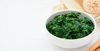 close up green cook leaf spinach salad in white bowl on white table background. leaves spinach or heap of spinach food salad photo