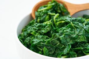 close up green cook leaf spinach salad in white bowl on white table background. leaves spinach or heap of spinach food salad photo