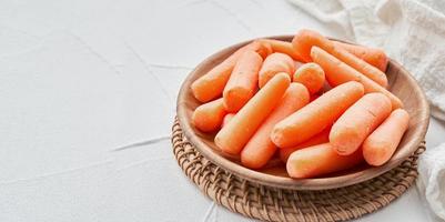 close up pile of baby small carrots in wood plate on white table background. small baby carrots, fresh baby carrots photo