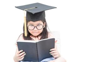 asiático colegio niño graduado leyendo libro con graduación gorra aislado foto