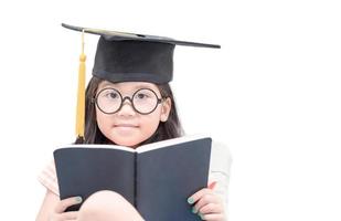 contento asiático colegio niño graduado leyendo libro con graduación gorra foto