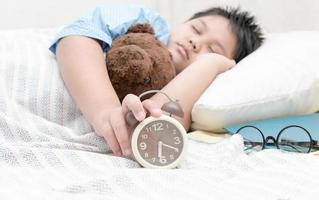 mano chico alcanzando a giro apagado alarma reloj en el cama. foto