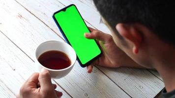 över huvudet se av innehav en kaffe kopp och använder sig av smart telefon med grön skärm video