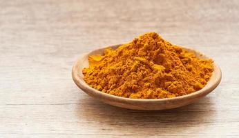 a pile of ground turmeric powder or curcumin powder in wood plate on wooden table background. turmeric or curcumin powder background photo