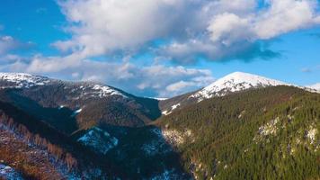 Hyper lapse of clouds running on blue sky over amazing landscape of snowy mountains and coniferous forest on the slopes video