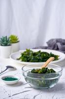 laminaria Kelp seaweed and spirulina powder in a glasses bowl with a wooden spoon on white background. vertical photo