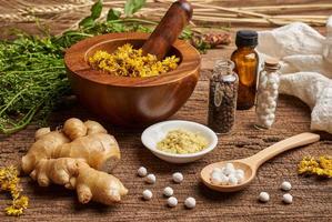 concept of homeopathic pills in a wooden spoon and bottles with the herb in a mortar with a pestle on wooden table background photo