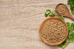 top view or flay lay dry coriander seed spice and leaf or leaves in wood plate and spoon on wooden table overhead background photo