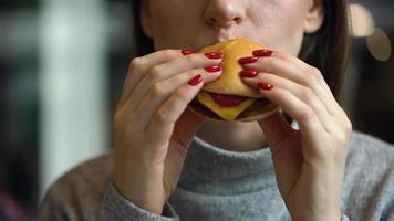 Woman eats a hamburger in a cafe video