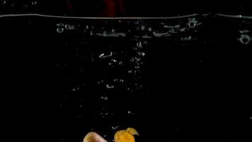 Baby carrots fall in water, black background, slow motion video