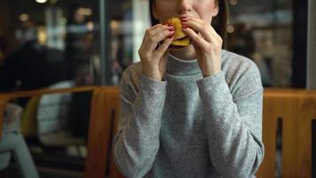 Woman eats a hamburger in a cafe video