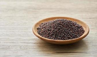 black mustard seed in wood plate on wooden table background. a pile of black mustard seed in wood plate on wooden table background. photo