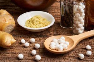 concept of homeopathic pills in a wooden spoon and bottles with herb on wooden table background photo