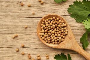 top view or flat lay dry coriander seed spice in wooden spoon and leaf or leaves on wood table background with copy space photo