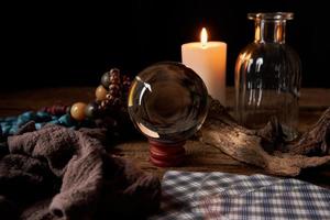 concept of fortune-telling on a wooden table and white candle with a crystal ball and tarot cards on dark background photo