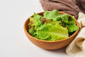 fresh salad from green leaves in a wooden bowl on white clean mood background with copy space. spoon and fork photo