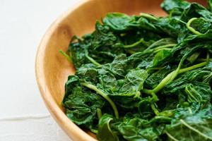 close up green cook leaf spinach salad in wood bowl on white table background. leaves spinach or heap of spinach food salad photo