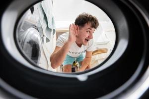 Man view from washing machine inside. Male does laundry daily routine. Listens to the sound inside. photo