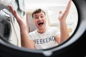 Man view from washing machine inside. Male does laundry daily routine. Satisfied expression on his face, spreading hands to the side. photo