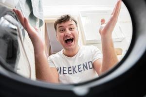 Man view from washing machine inside. Male does laundry daily routine. Satisfied expression on his face, spreading hands to the side. photo