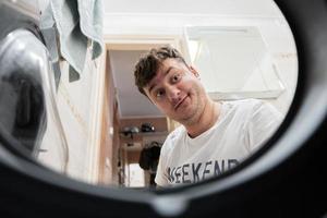 Man view from washing machine inside. Male does laundry daily routine.  Surprised facial expression. photo