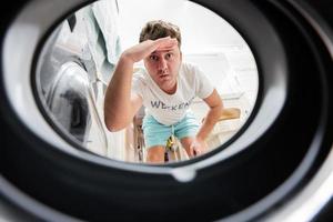 Man view from washing machine inside. Male does laundry daily routine. Hand over forehead looking far away, watching or searching. photo