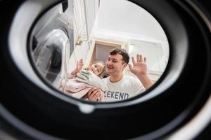 Man and girl view from washing machine inside. Father with daughter does laundry daily routine. photo