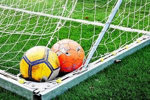 two ragged shabby soccer balls in the corner of the football goal net photo