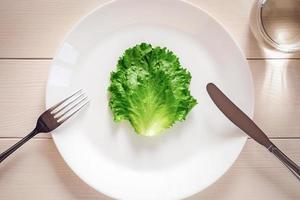 Green lettuce leaf on a plate, fork, knife, glass of water - strict diet concept photo