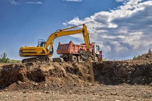 Yellow excavator and empty truck working at the construction site photo