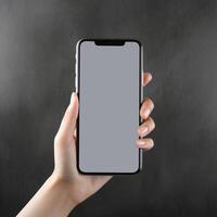 hand holding smartphone with blank screen on gray background. Mock up , photo