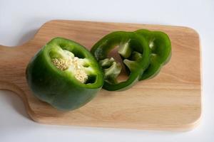 Cutting green sweet bell pepper on the wooden board isolated on white background. photo