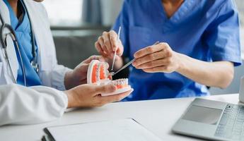 dentista sentado a la mesa con muestras de mandíbula modelo de diente y trabajando con tableta y computadora portátil en el consultorio dental clínica dental profesional. medico trabajando foto