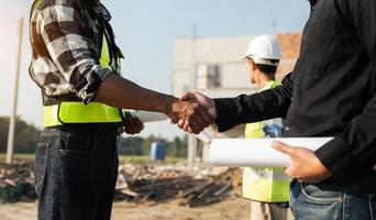 Construction team shake hands greeting start new project plan behind yellow helmet on desk in office center to consults about their building project. photo