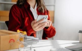mujer joven sosteniendo un teléfono inteligente que muestra el éxito del pago y la tarjeta de crédito con una caja de paquetes amarilla como concepto de compras en línea foto