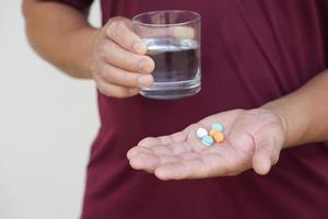 Man holds pills and glass of water to take medicine. Concept Health care, health problem, sickness and remedy. Basic self take care , treatment at home when get sick. Take pills under prescription. photo