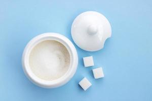 open sugar bowl with sugar next to cubes of refined sugar on a blue background photo